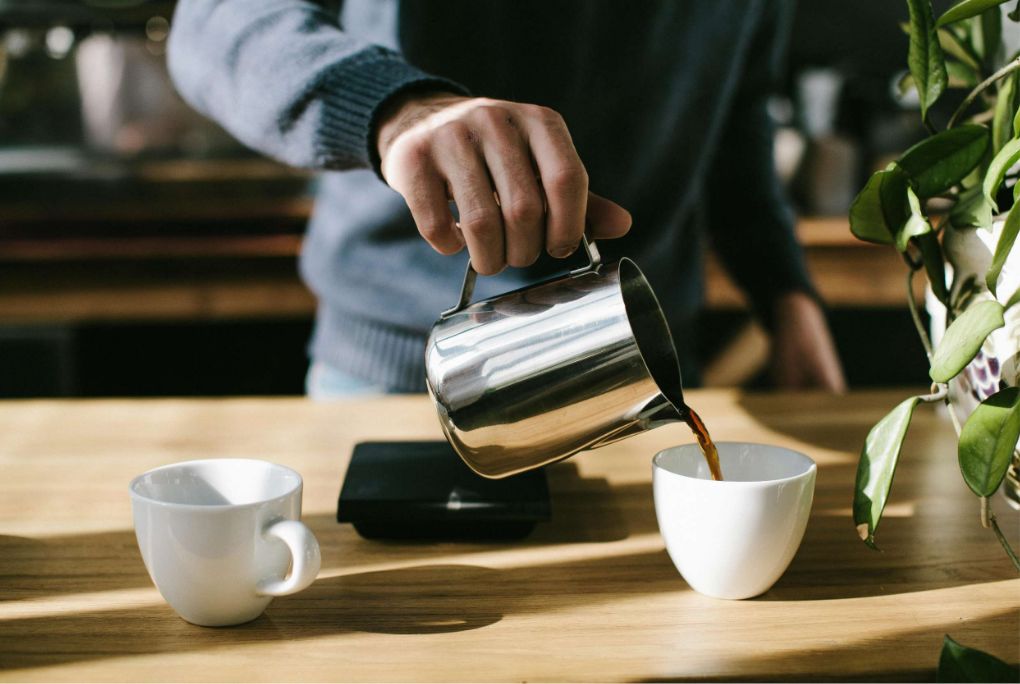 A person pouring coffee from a pot into two cups on a table, creating a warm and inviting atmosphere