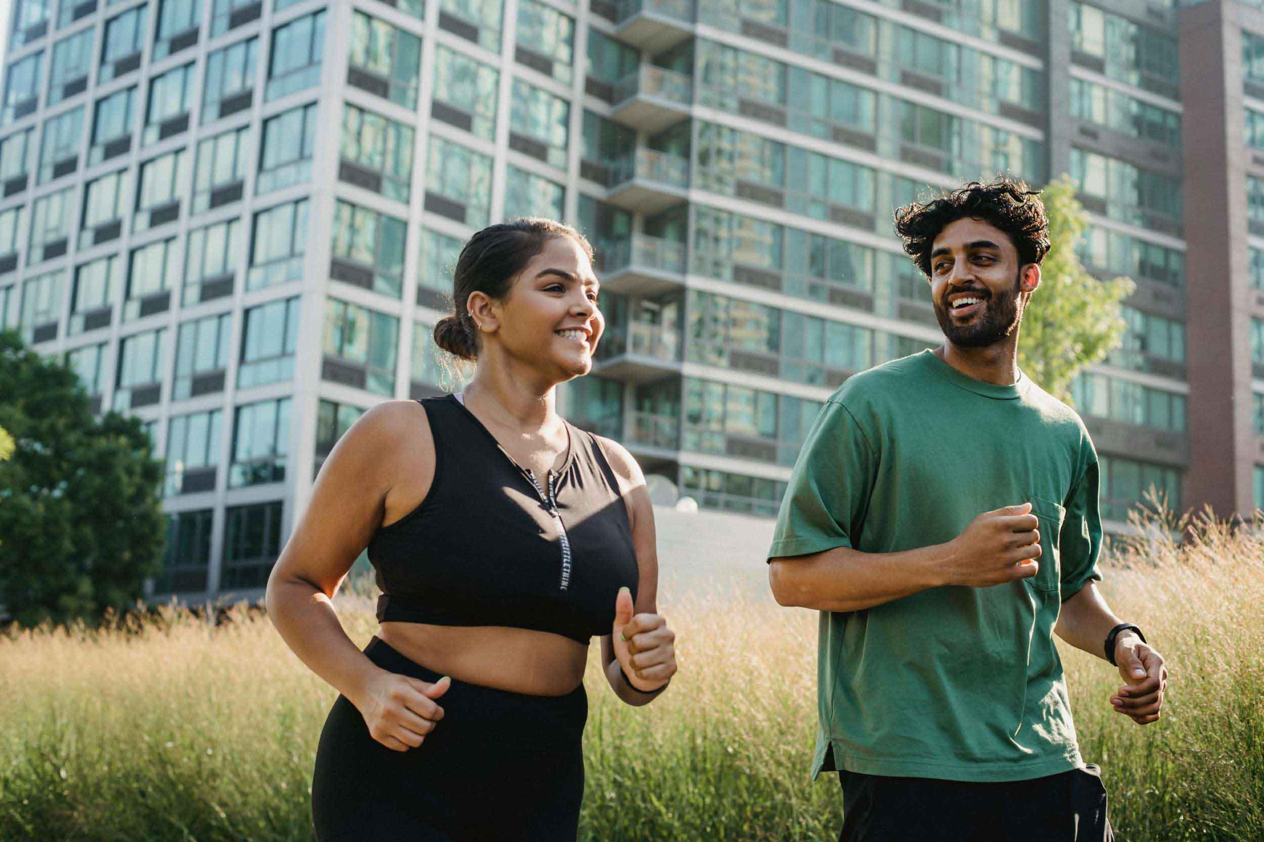 A man and woman jogging together in a park, surrounded by greenery and a clear blue sky