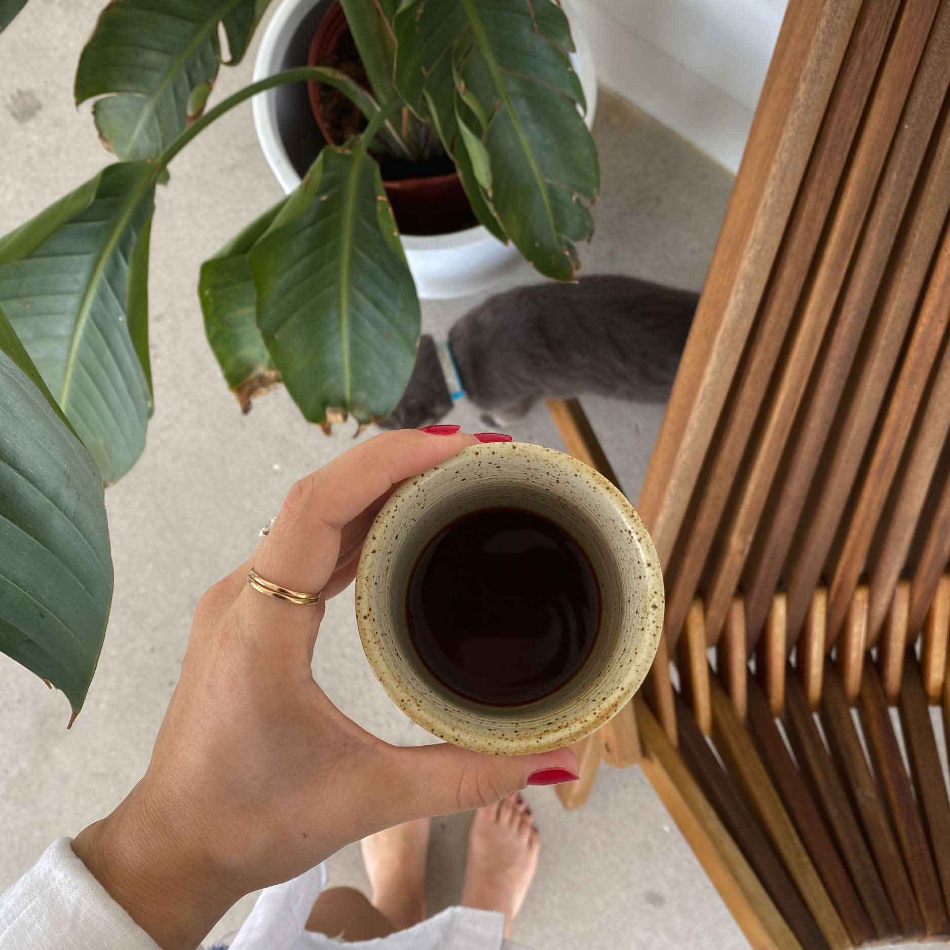 A person enjoying a cup of coffee alongside a lush plant, evoking a sense of calm and tranquility