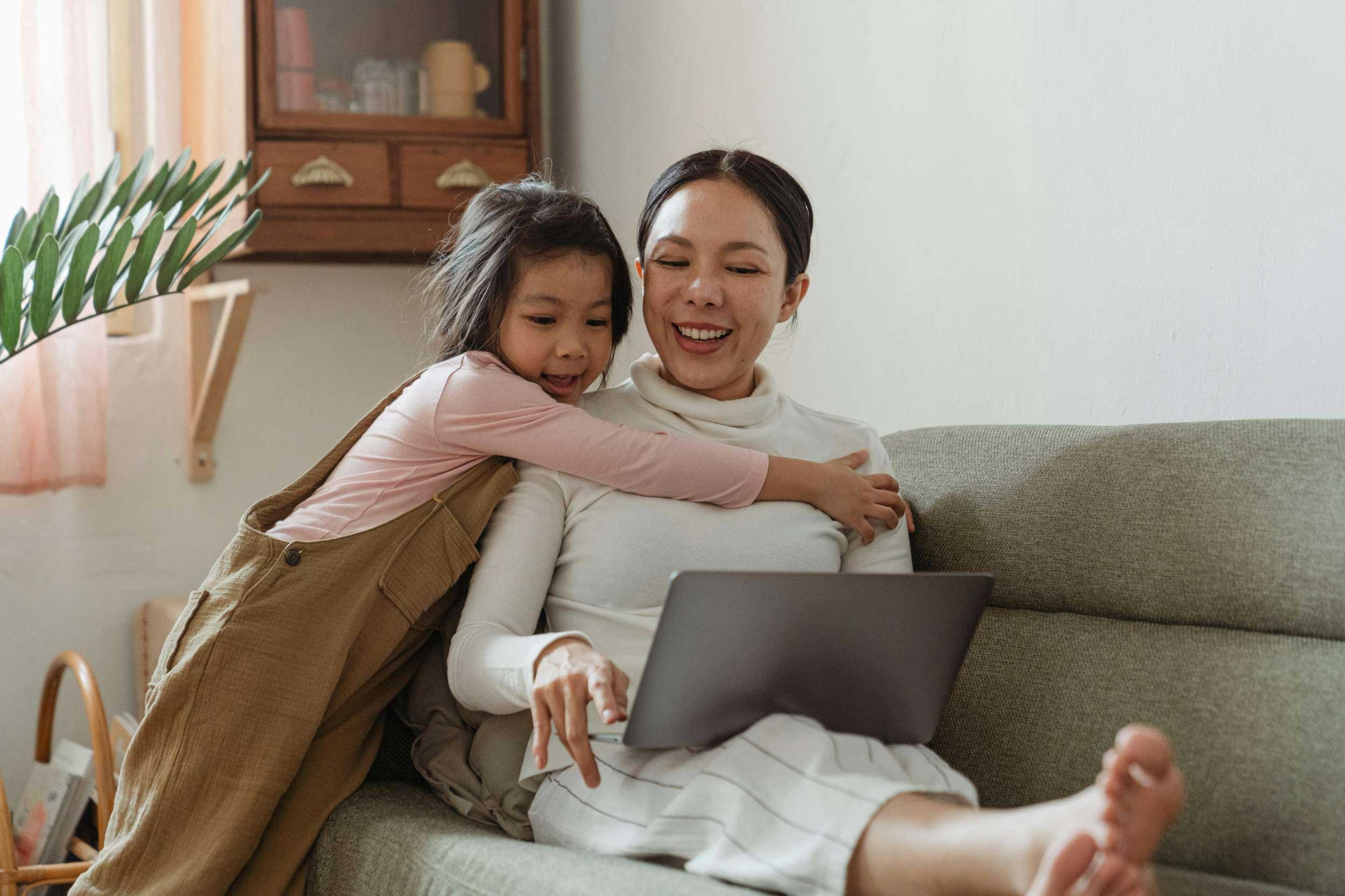 Blog 2 A woman and a child are seated on a couch, engaged with a laptop, sharing a moment of learning and connection