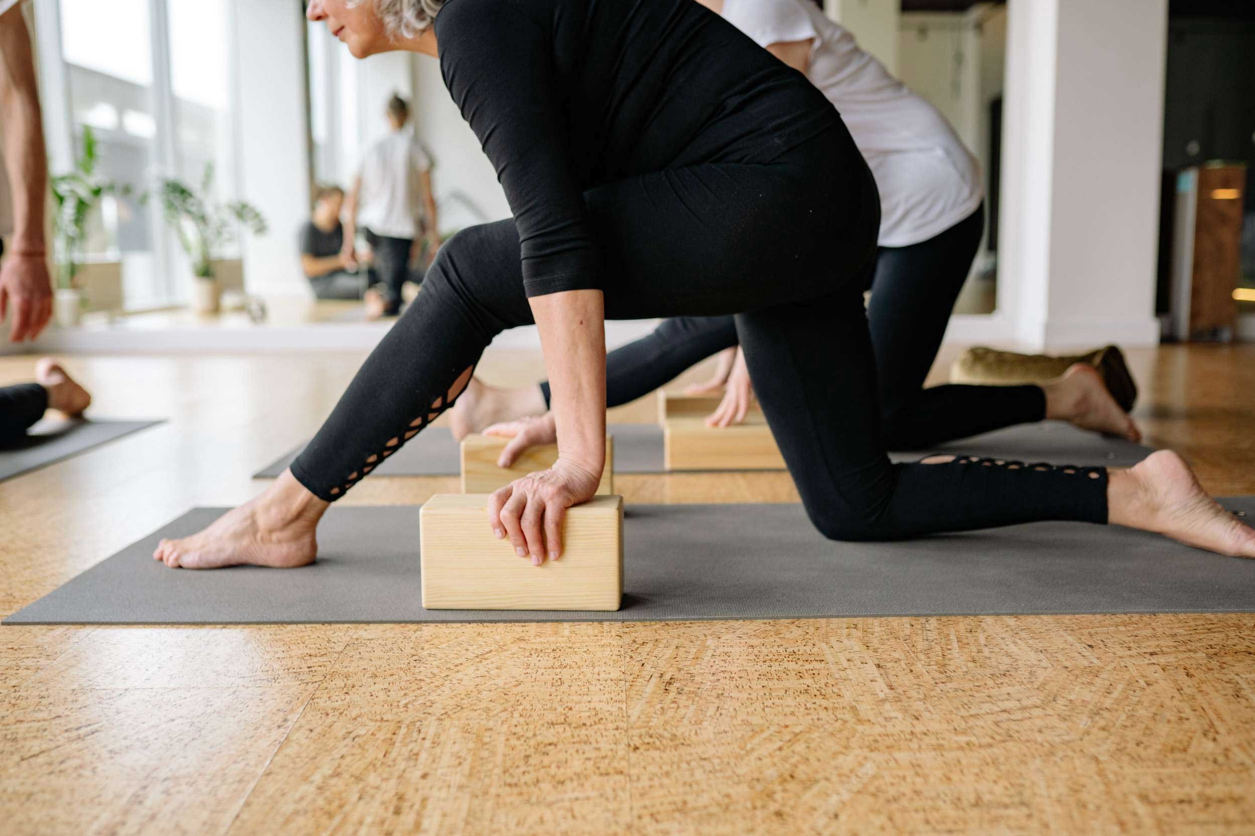 A woman practices yoga on a mat, using a block for support in a serene indoor setting