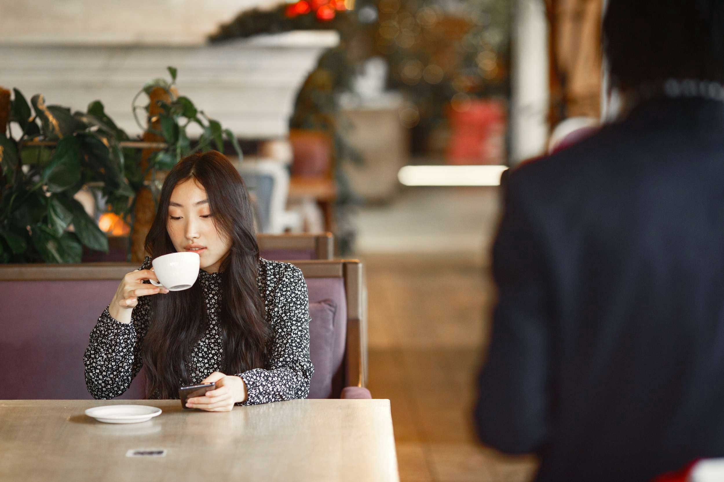 A woman seated at a table, enjoying a cup of coffee in a cozy setting.