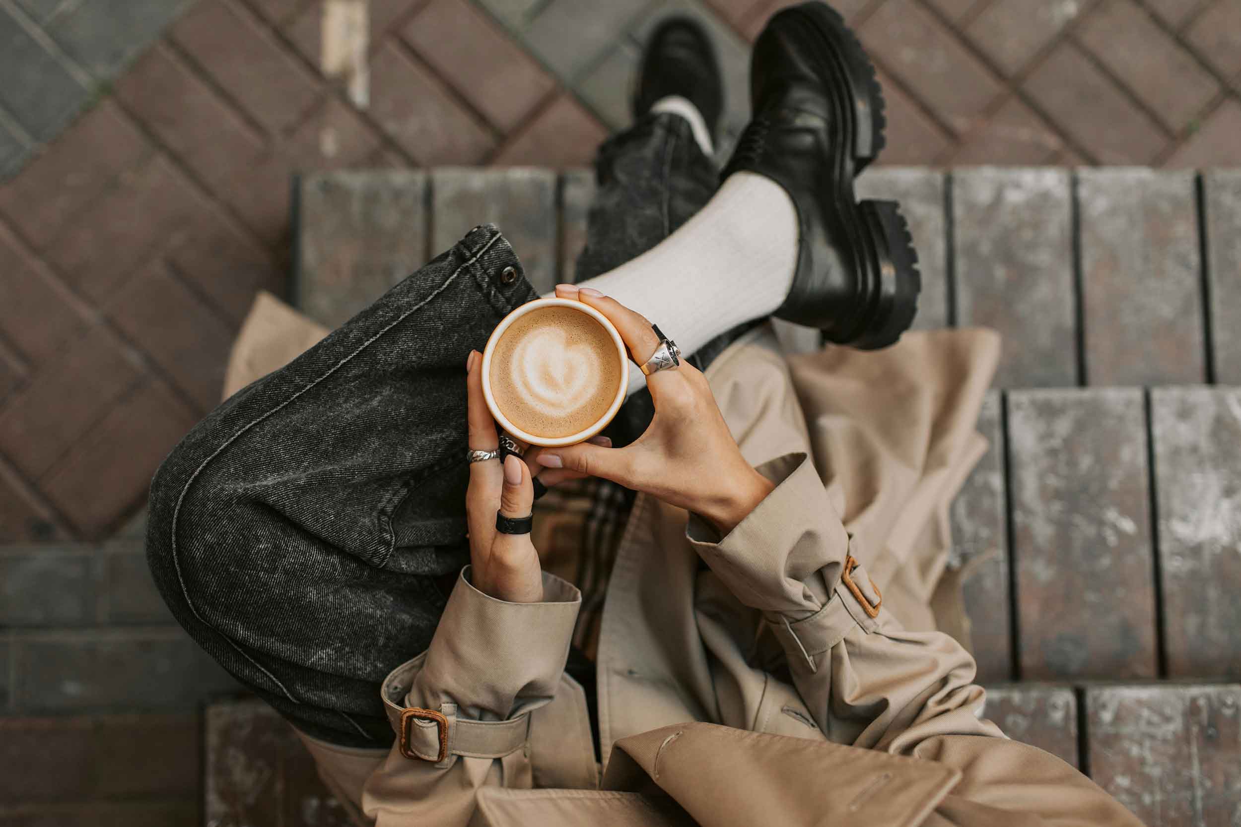 A person seated on a wooden bench, enjoying a cup of coffee in a serene outdoor setting