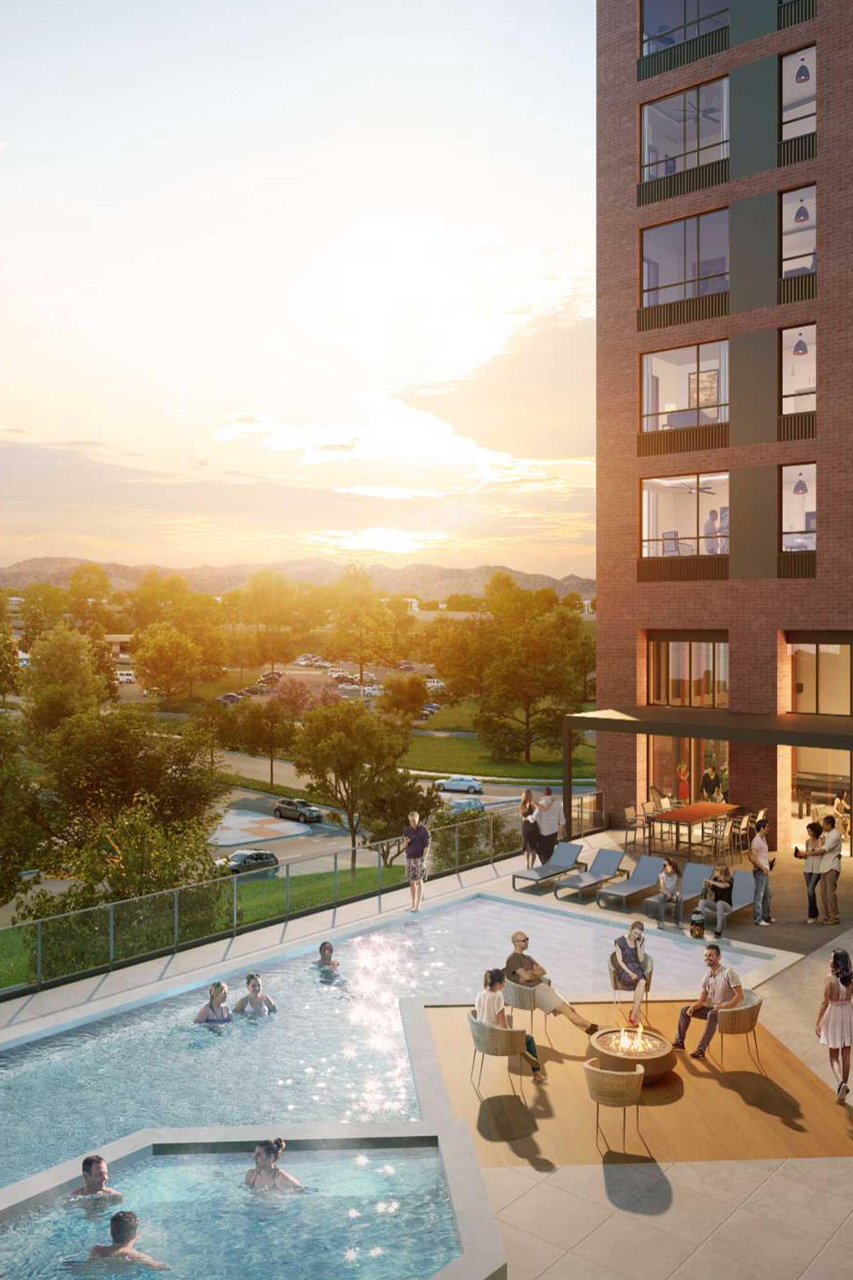 People relax and socialize around a pool and fire pit on the outdoor terrace of a modern apartment building at sunset.