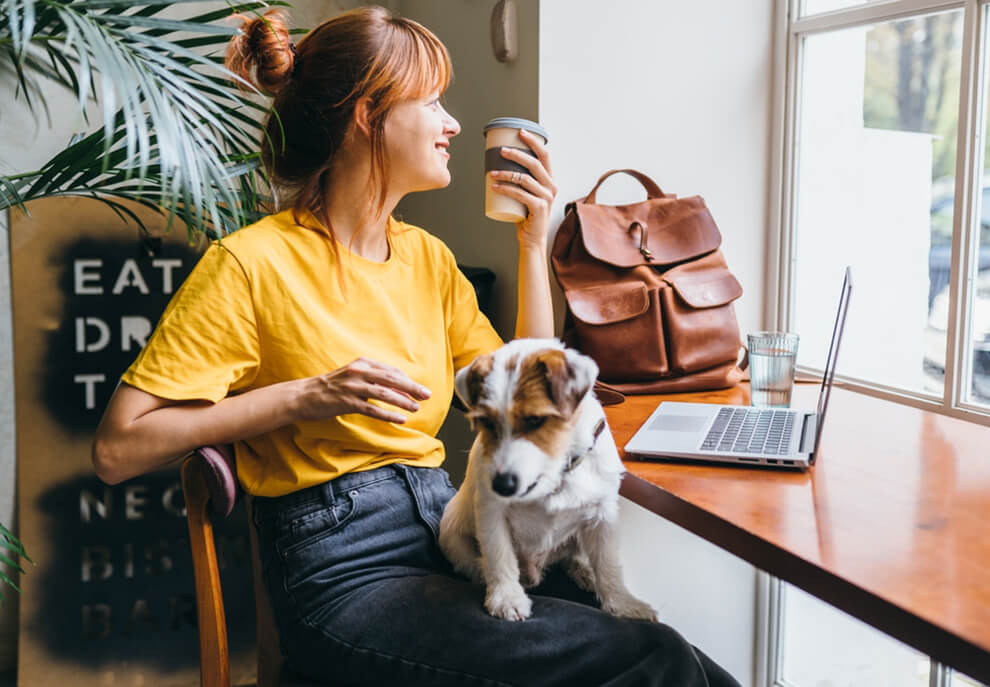 Dog-Friendly Coworking Spaces in Denver 3 A woman sitting at a café table with her dog on her lap, holding a coffee cup.