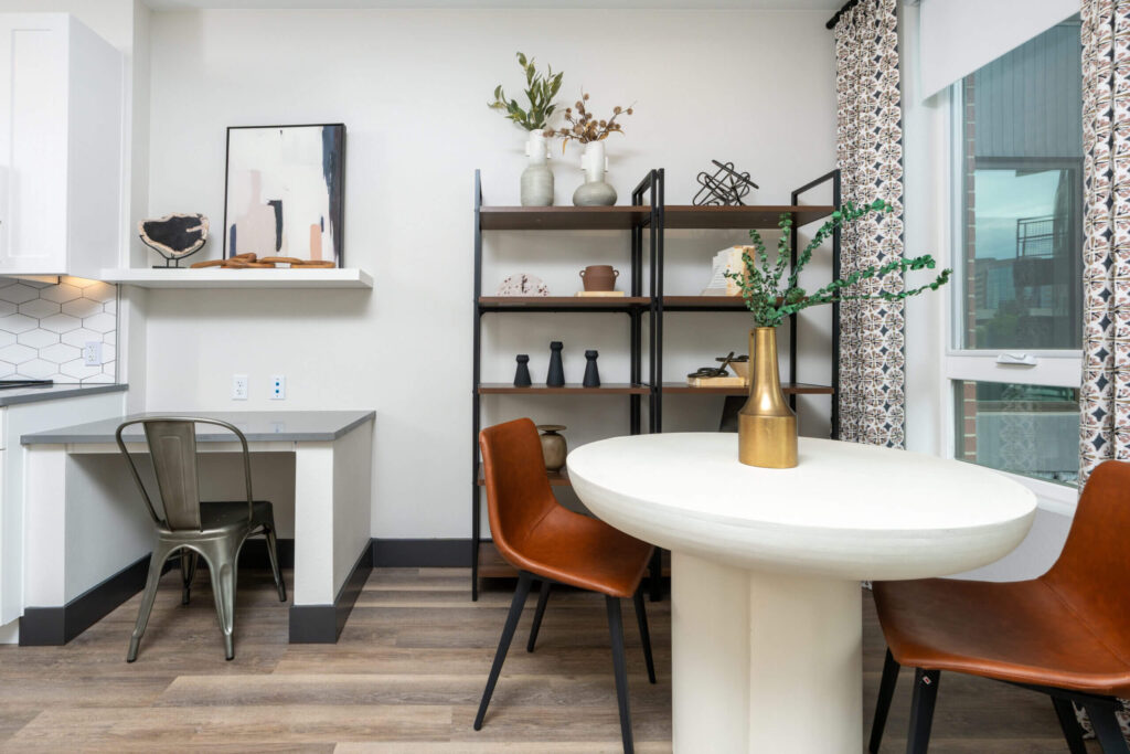 Modern apartment dining area with a round white table, brown leather chairs, open shelving, and a small built-in desk.
