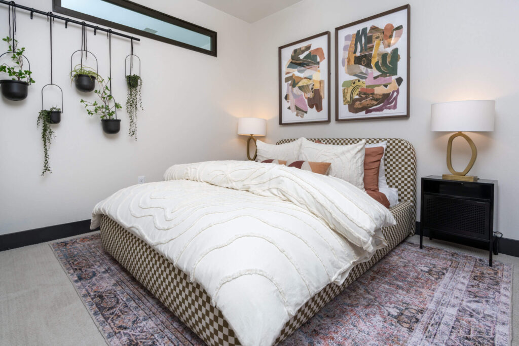 Three Bedroom Luxury Apartments in Denver, CO 1 Modern bedroom with a patterned bed, white bedding, wall art, hanging plants, and bedside lamps.